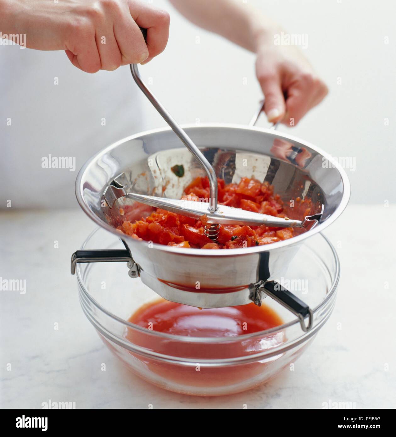 Mit einem Essen Mühle Tomaten über Glas Schüssel zu Püree, close-up Stockfoto