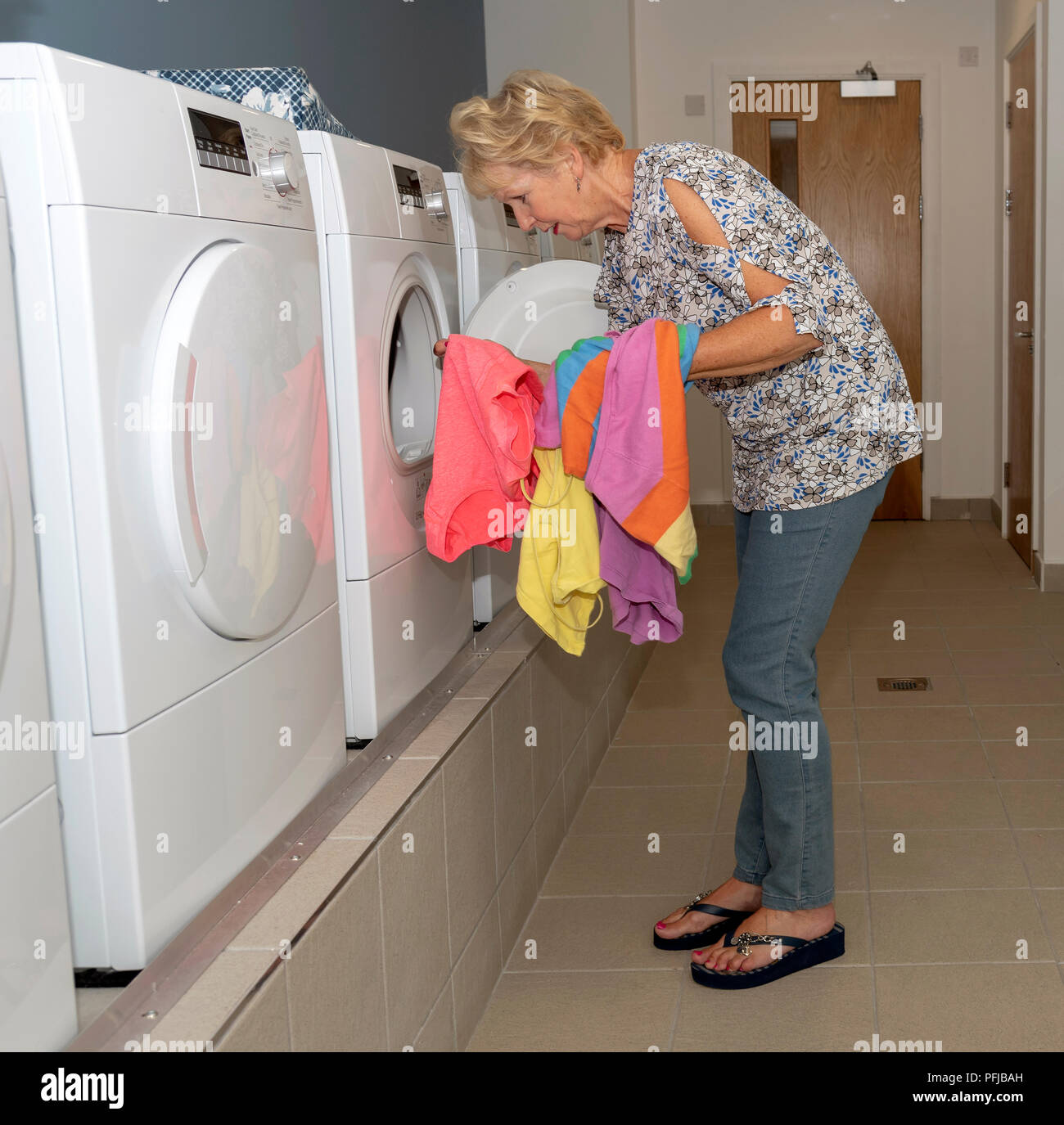 Ältere woamn Entfernen getrocknete Kleidung von einem Trockner in einem Waschraum Stockfoto