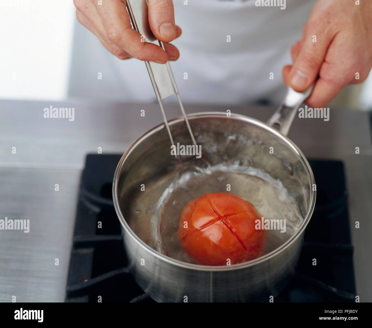 Hand, die Tomate in Sieb innen Topf kochendes Wasser auf einem Herd Stockfoto