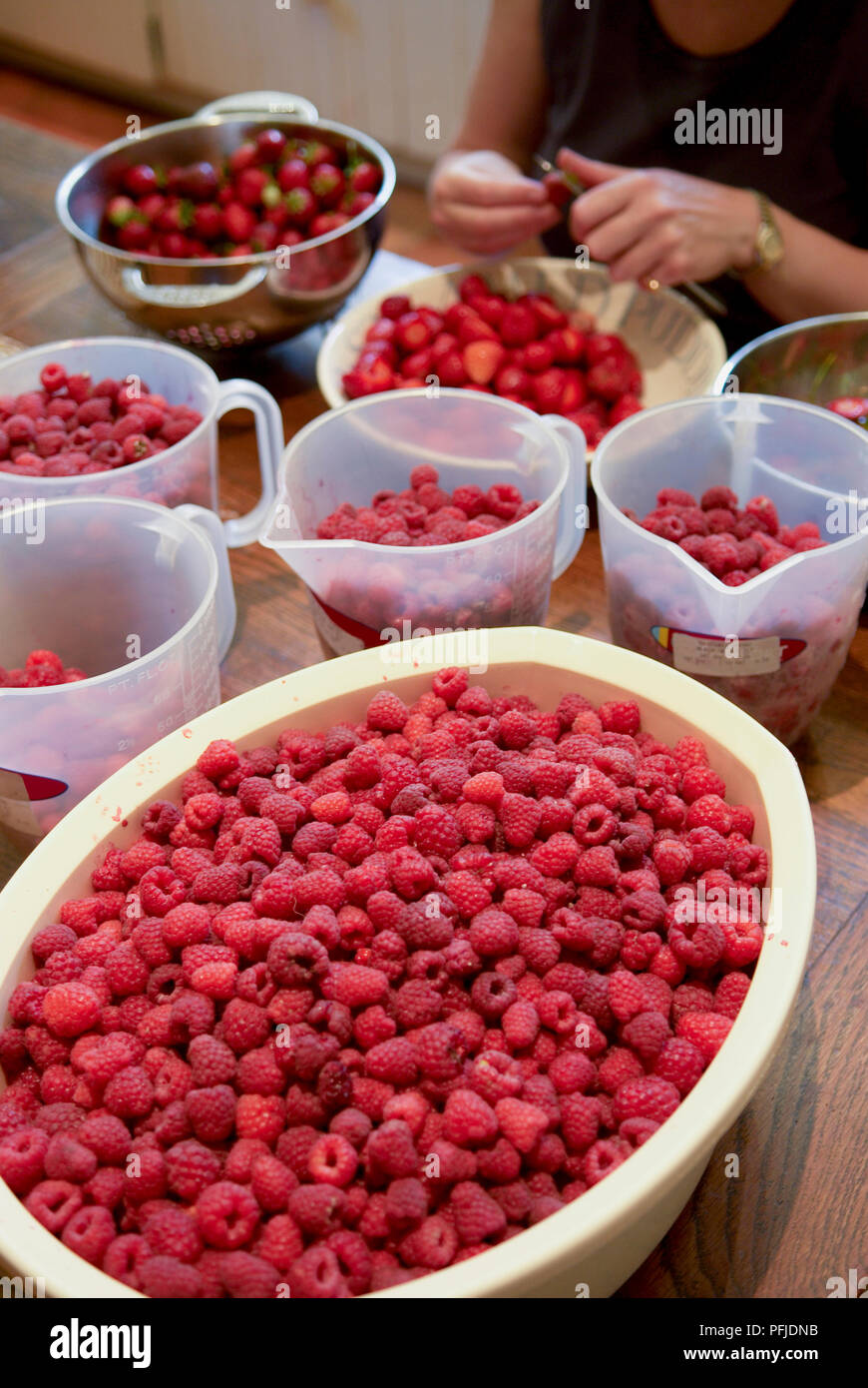 Container gefüllt mit Himbeeren und Erdbeeren, Frau schneiden Erdbeeren im Hintergrund, Nahaufnahme Stockfoto