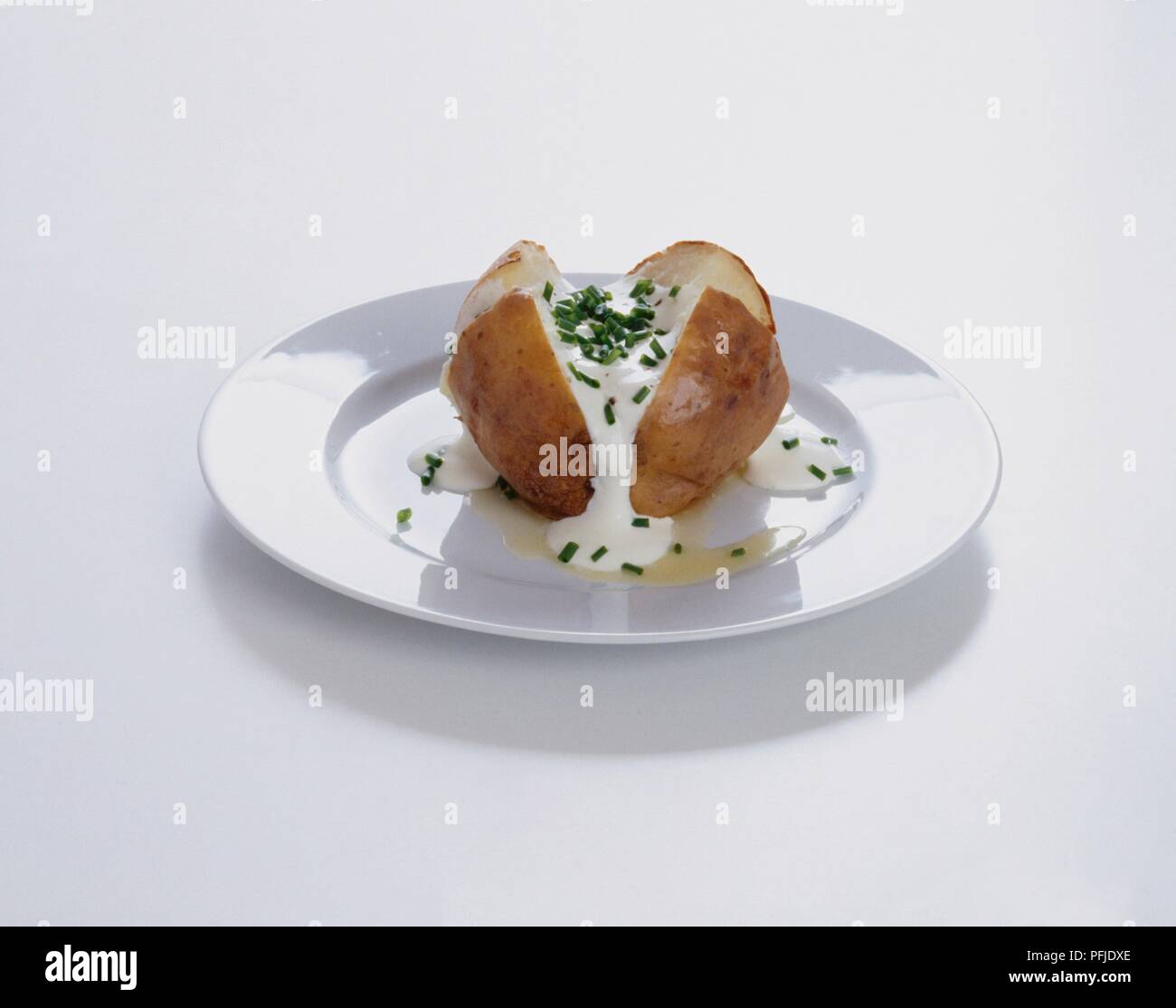 Gebackene Kartoffeln mit saurer Sahne und Schnittlauch auf weiße Platte Stockfoto