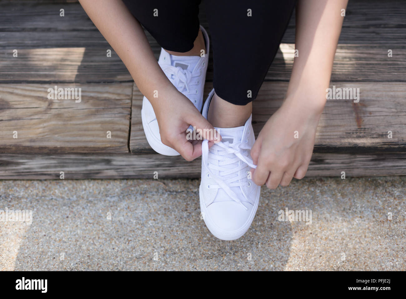 Junge Frau Riegel Schnürsenkel auf weißen Turnschuhen auf hölzernen Deck Stockfoto