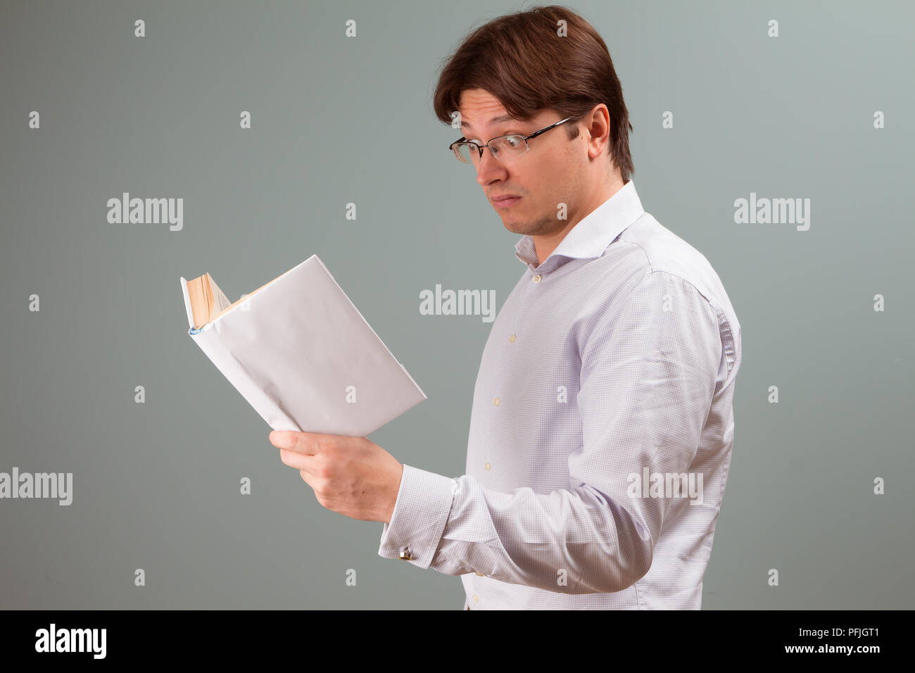 Ein junger Mann, der auf einem Buch in Weiß Abdeckung fokussiert, mit überrascht Emotion auf dem Gesicht; horizontale Ausrichtung studio Portrait. Stockfoto