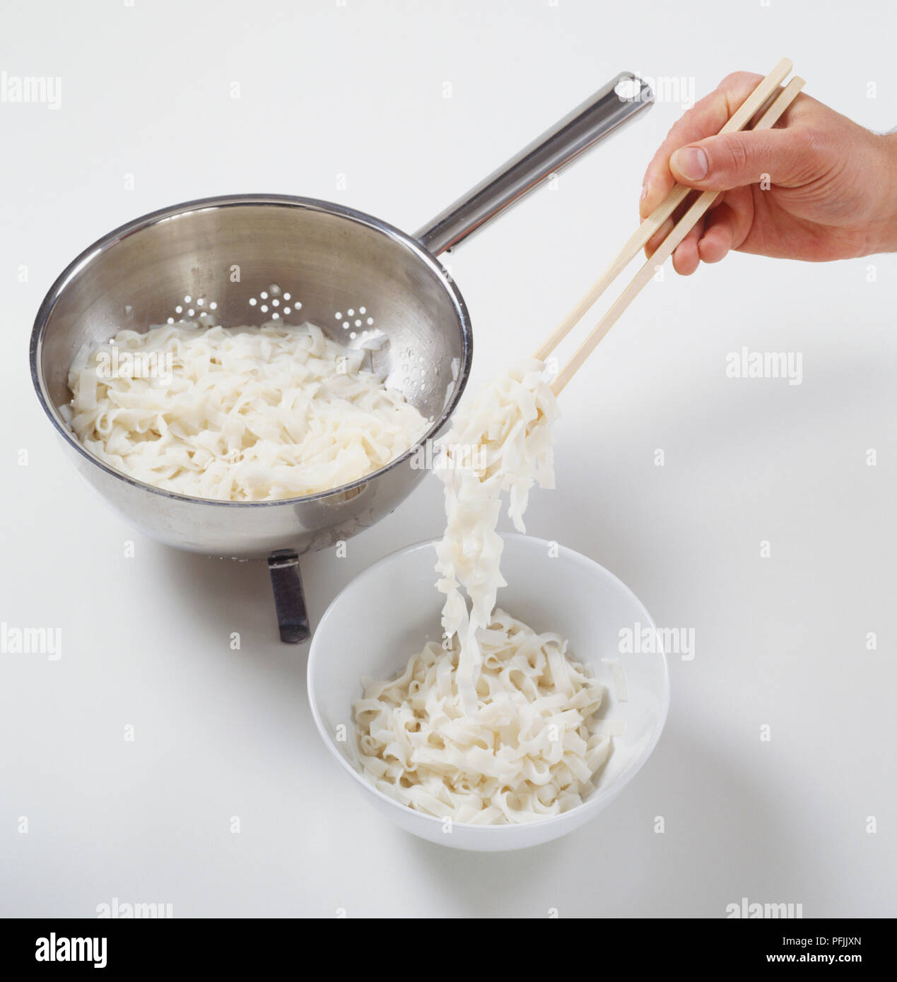 Mit Stäbchen gekochten Reis Nudeln vom Sieb in die Schüssel zu bewegen, hohe Blickwinkel betrachten. Stockfoto