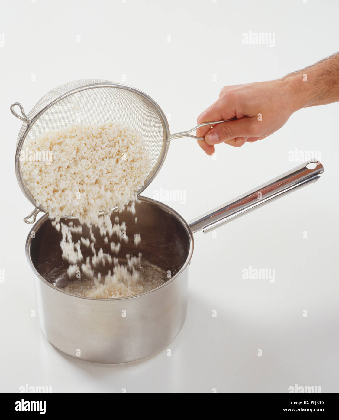 Gießen gewaschenen Reis vom Sieb in den Topf gefüllt zu einem Drittel mit Wasser, verschwommene Bewegung. Stockfoto