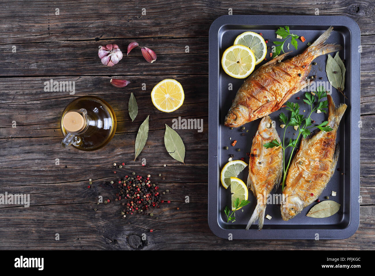 Lecker gebratene Dorade Fisch mariniert mit Zitronenscheiben, Lorbeerblatt, Gewürze auf Backblech auf alten, dunklen rustikalen Tisch mit Zutaten auf Hintergrund, hor Stockfoto