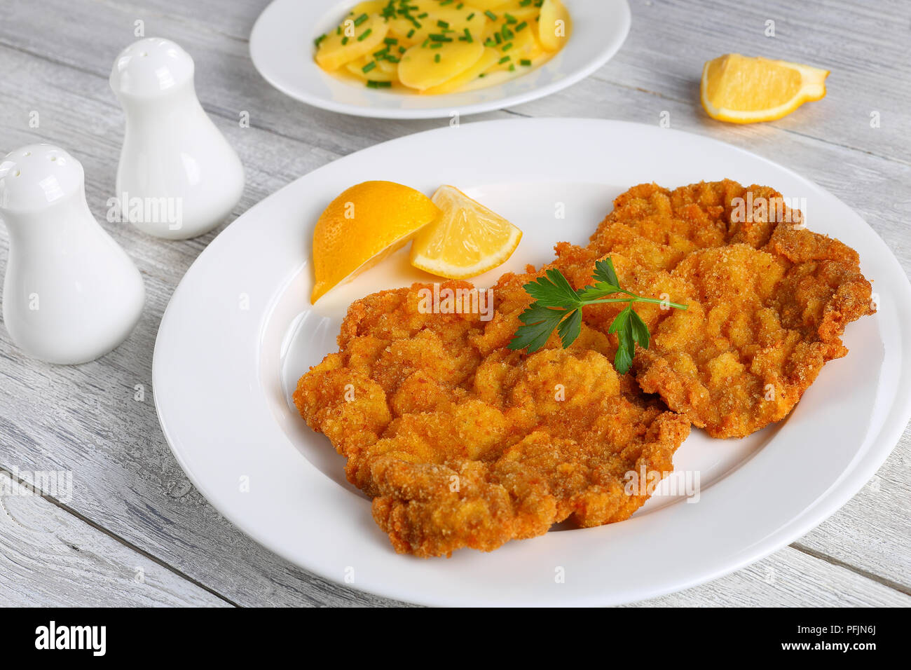 Köstliche golden braun klassisches Wiener Schnitzel- oder paniertes Schnitzel serviert auf weiße Platte mit Zitronenscheiben auf dunklen Holztisch mit Glas r Stockfoto