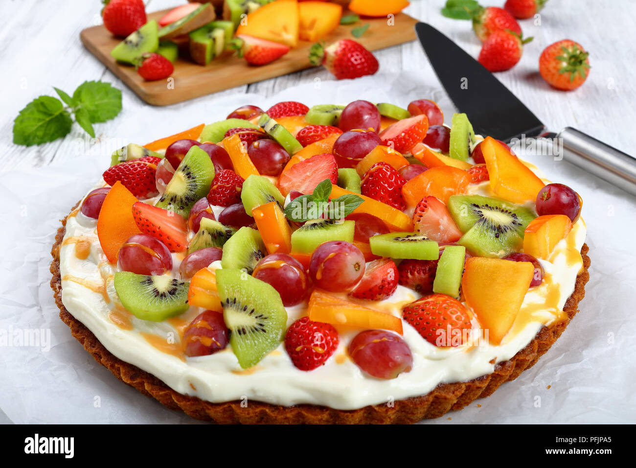 Pumpkin Torte mit Frischkäse, dekoriert mit Trauben, Kiwi, Erdbeere und Kaki, beträufelt mit Kürbis ganache auf Papier. pie Heber und Cu Stockfoto