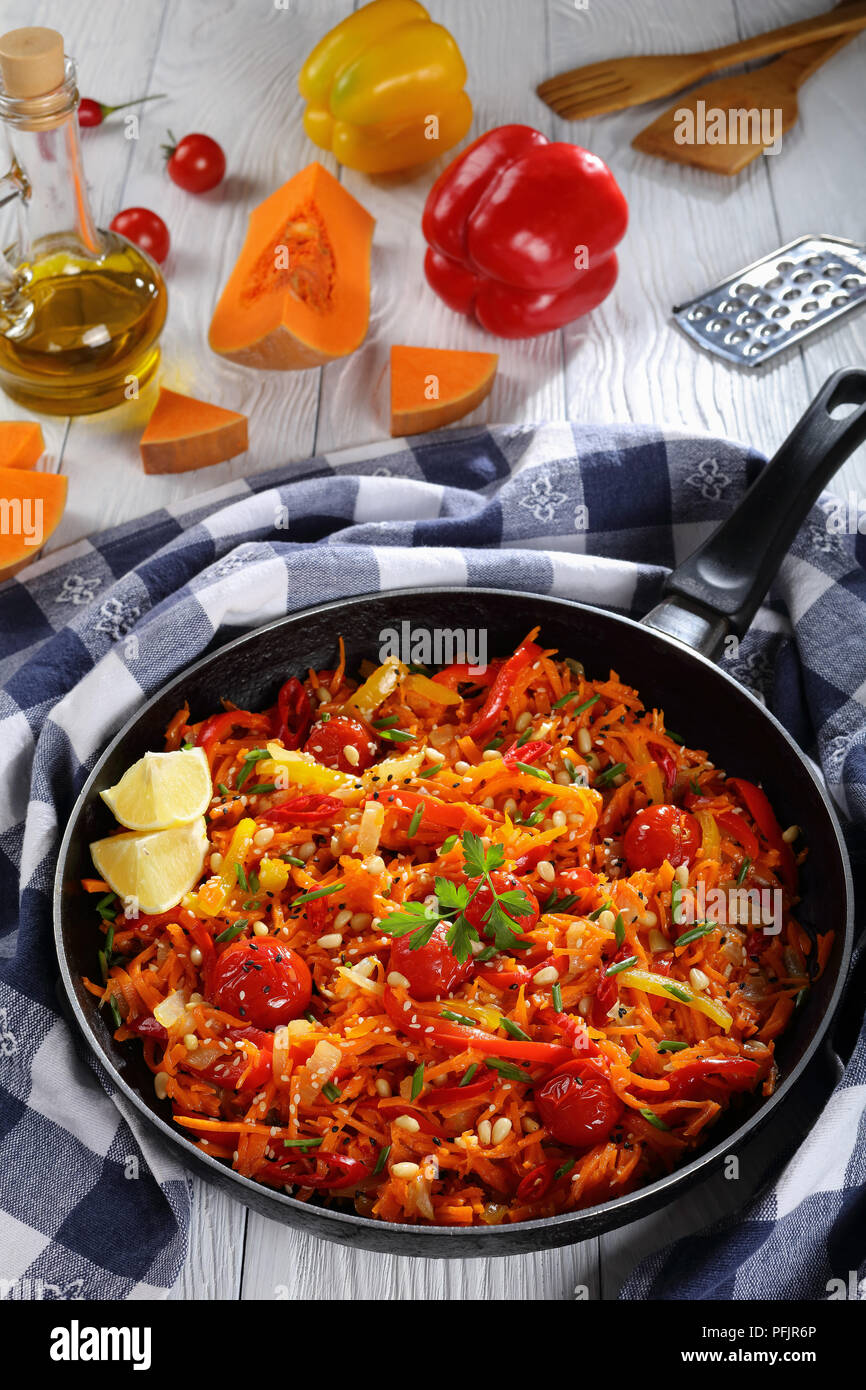 Ein Topf, Teller - Hot pumpkin Salat mit Tomaten, Paprika, Zwiebel, bestreut mit Sesam und die Pinienkerne in einer Pfanne mit Zutaten auf Backgr Stockfoto