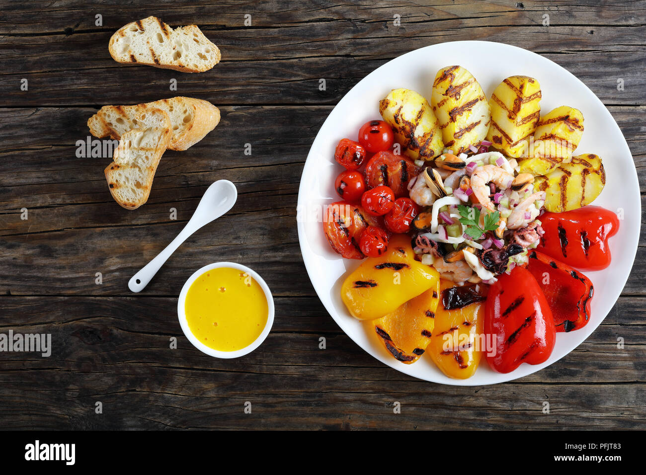 Lecker spicy Seafood Salat beträufelt mit Zitronensaft serviert auf weiße Platte mit gegrilltem Gemüse. basic rue Sauce und geröstetem Baguette auf Holz Stockfoto