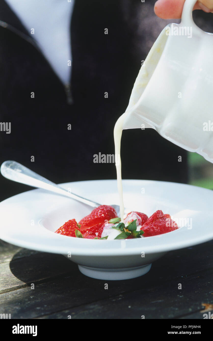 Creme von Kanne über Schüssel mit frischen Erdbeeren, Seitenansicht Stockfoto