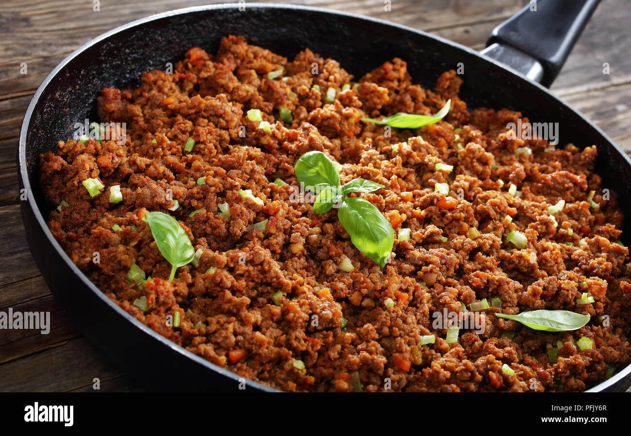 Leckere heiße Fleisch Ragout bolognese mit Tomatensauce, fein Gemüse und Kräuter in der Pfanne auf alten Holztisch gehackt, klassische Zutat für in der Vergangenheit Stockfoto