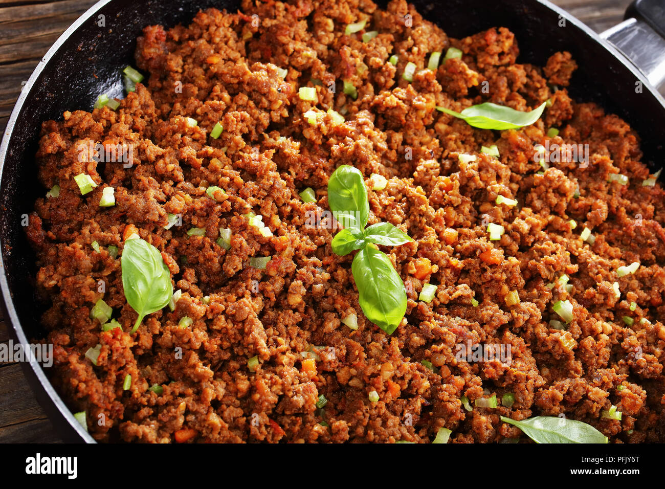 In der Nähe von köstlichen warmen Fleisch Ragout bolognese mit Tomatensauce, Basilikum, fein gehackt Gemüse und Sellerie in Skillet auf alten hölzernen Tisch, Blick fr Stockfoto
