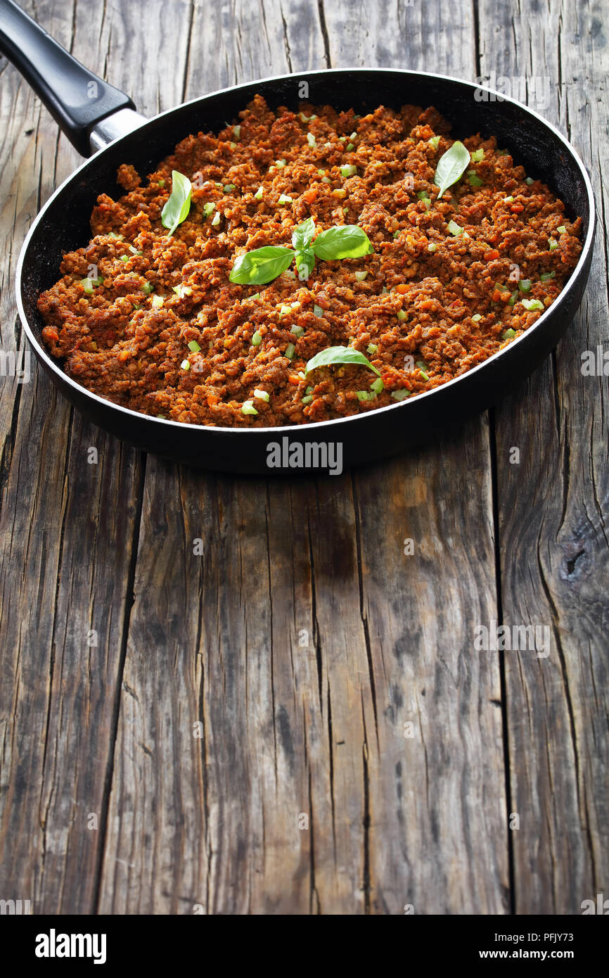 Hot saftiges Fleisch Ragout bolognese mit Tomatensauce, Basilikum, fein gehackt Gemüse und Sellerie in Skillet auf alten Holztisch, klassisches Rezept, vertica Stockfoto