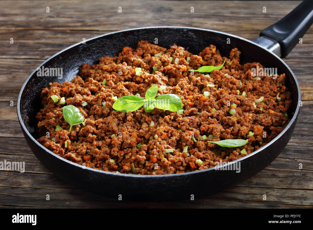 Hot Juicy Rinderhackfleisch geschmort mit Tomatensauce, Gewürze, Basilikum, fein gehackt Gemüse und Sellerie in der Pfanne, klassisches Rezept, Seitenansicht von abov Stockfoto