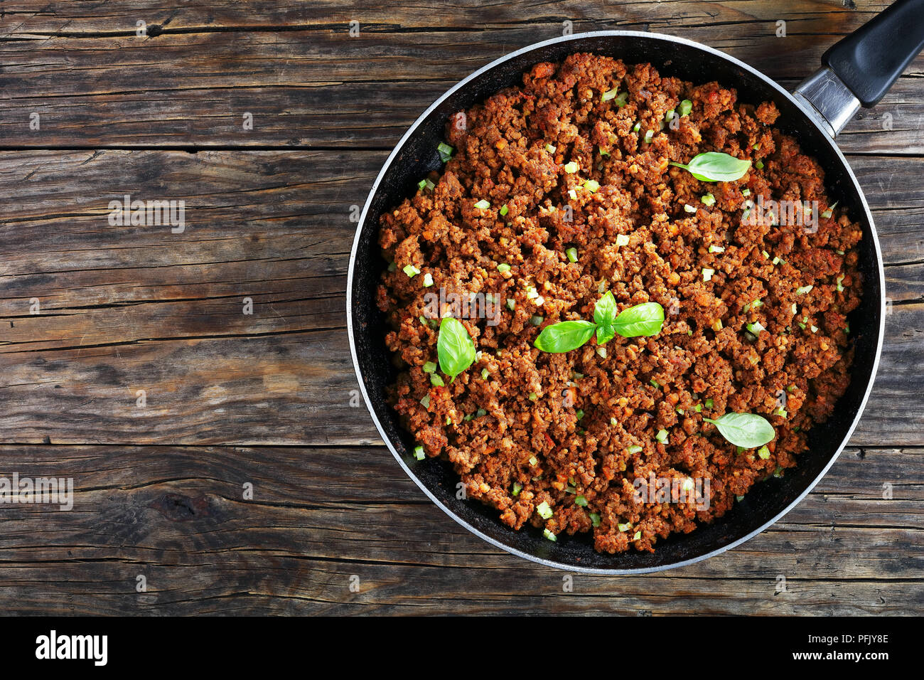 Bolognese Sauce - Hot Juicy Rinderhackfleisch geschmort mit Tomatensauce, Gewürze, Basilikum, fein gehackt Gemüse und Sellerie in Skillet auf Holztisch, Auth Stockfoto