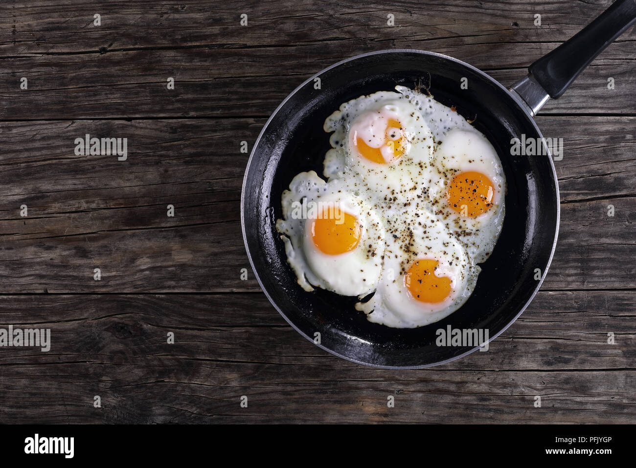 Spiegeleier gebraten auf Pfanne, mit gemahlener schwarzer Pfeffer bestreut, Ansicht von oben Stockfoto