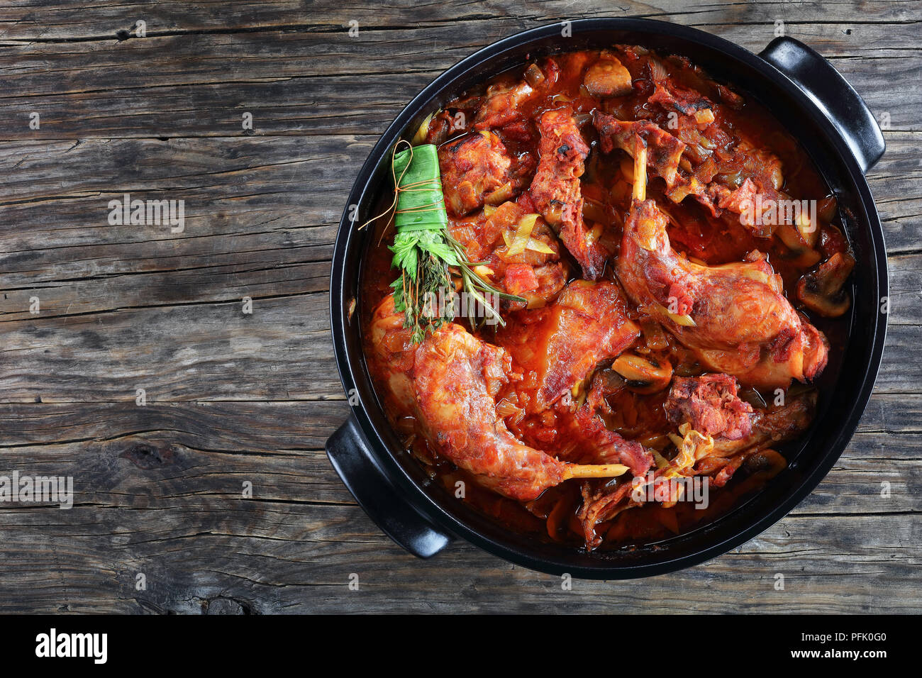 Italienisches geschmortes Kaninchen mit Lauch, Tomaten, Kräutern und Pilzen in holländischen Ofen auf alten, dunklen Holztisch gehackt, Ansicht von oben Stockfoto
