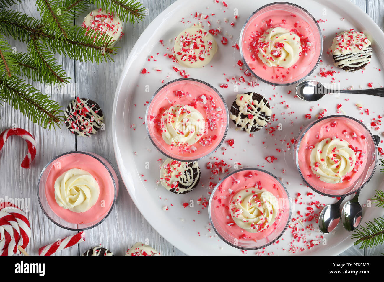 In der Nähe von Weihnachten keine Käsekuchen backen Mousse garniert mit Sahne, bestreut mit zerquetschten Zuckerstangen in Glas Tassen auf Tablett mit Tannenzweigen, Stockfoto
