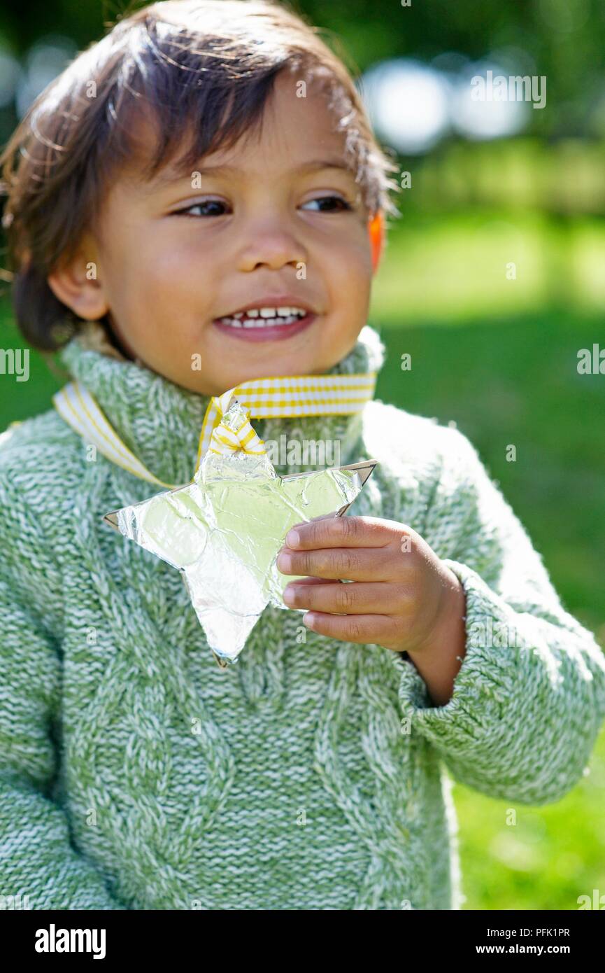Junge in wooly Jumpers, holding Sterne angebracht um den Hals zu Farbband Stockfoto