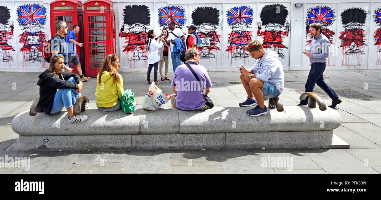 Touristen in St Martin's Place, London, England, UK. Traditionelle rote Telefonzellen und Graffiti Wachposten durch Künstler Nathan Bowendecorating constructi Stockfoto