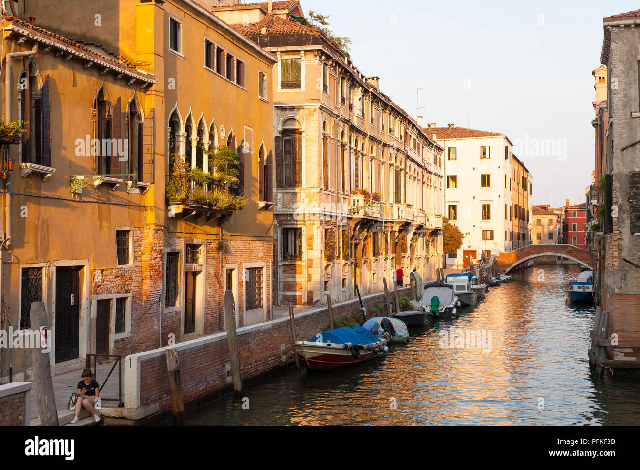 Rio di Santa Caterina, Cannaregio, Venedig, Venetien, Italien während der Goldenen Stunde bei Sonnenuntergang mit Reflexionen über den Kanal und die Boote, Mädchen mit Mobile auf St Stockfoto