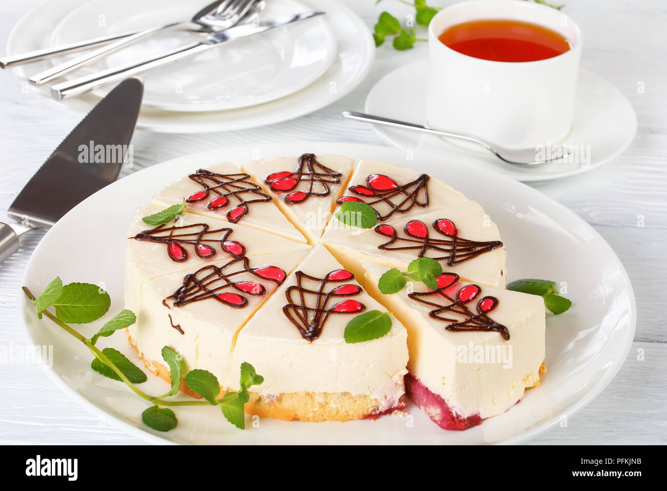 Leckeren Käsekuchen mit untere Schicht besteht aus biskuitteig mit Sweet berry Soße getränkt, auf weissem platter auf Holztisch, Tasse Kaffee und Pla Stockfoto