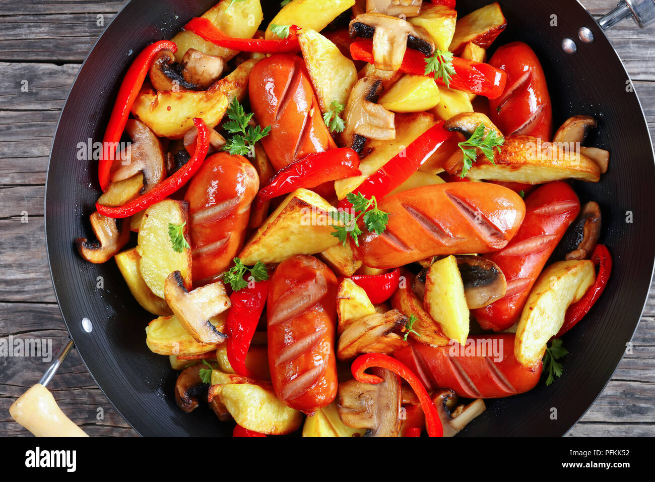 Hot gegrillte Würstchen mit Kartoffelecken, rote Paprika, Champignons und Petersilie in einer Pfanne, horizontale Ansicht von oben, close-up Stockfoto