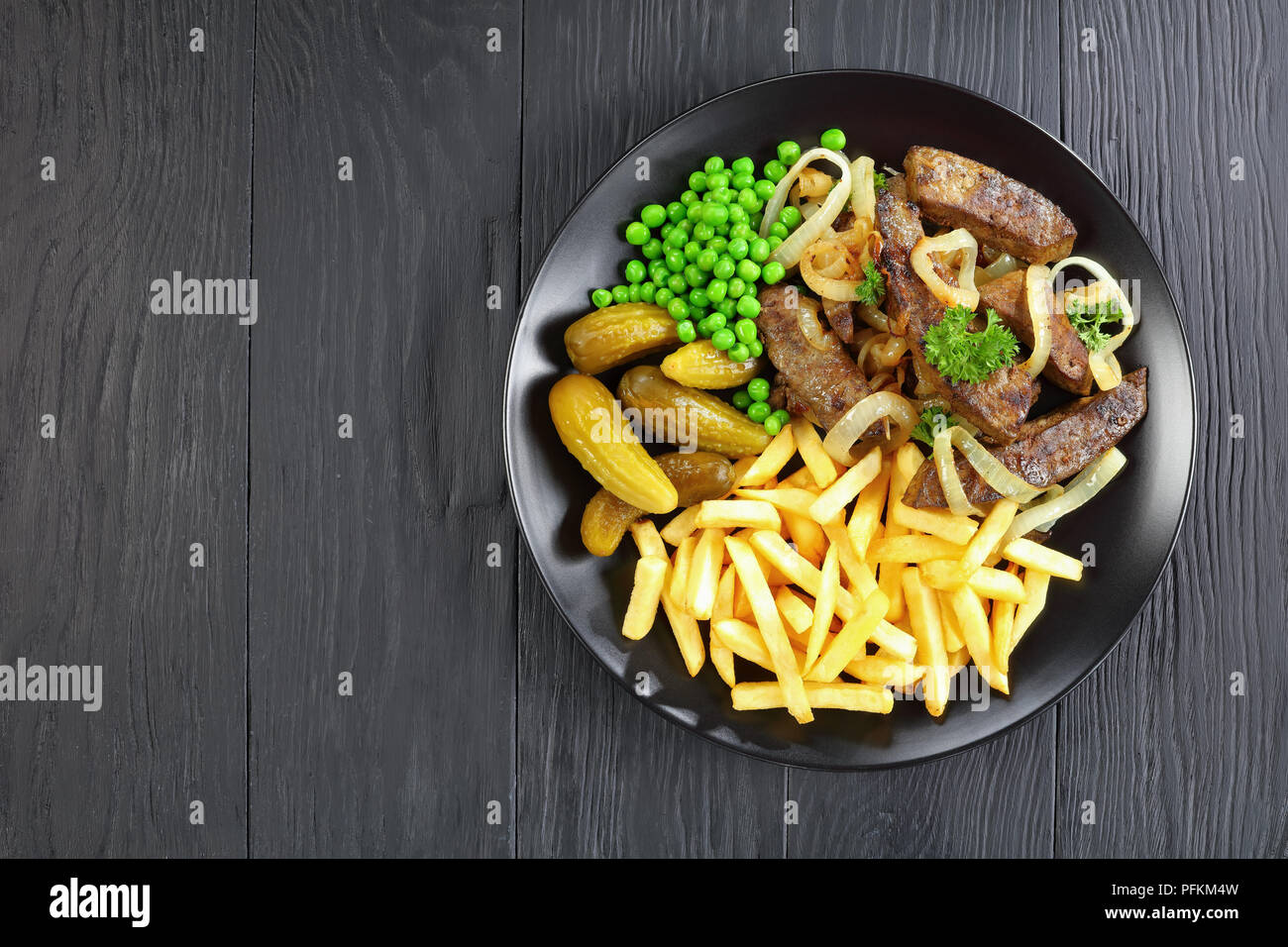 Lecker gebratene Kalbsleber mit Pommes, eingelegte Gurken, grüne Erbsen ...