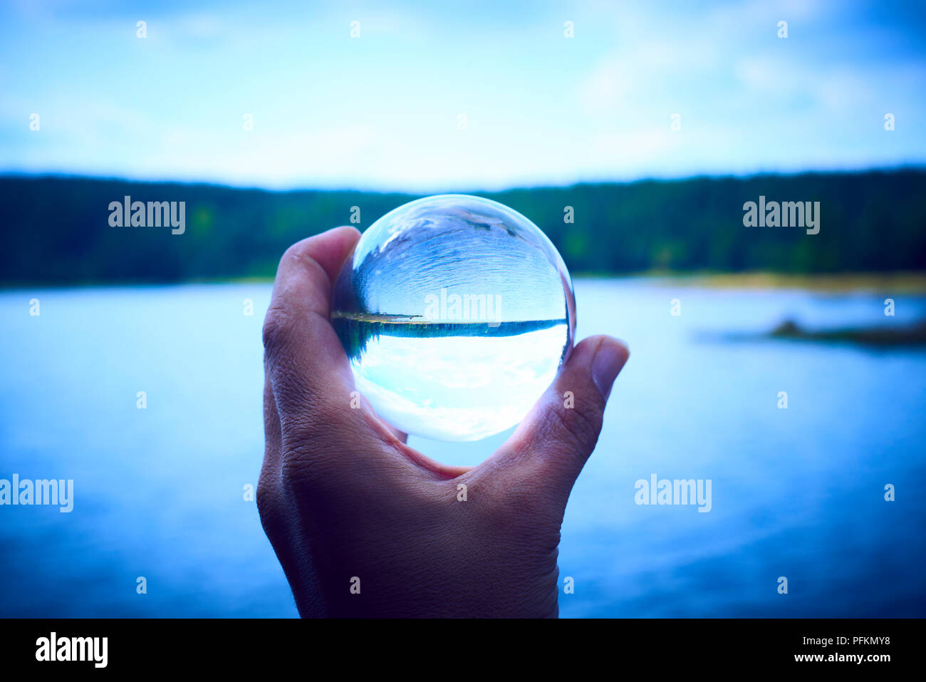 Hand mit einem Glas Kugel spiegelt den See und den Wald. Konzept der Umwelt, Naturschutz, Ökologie. Selektiver Fokus Stockfoto