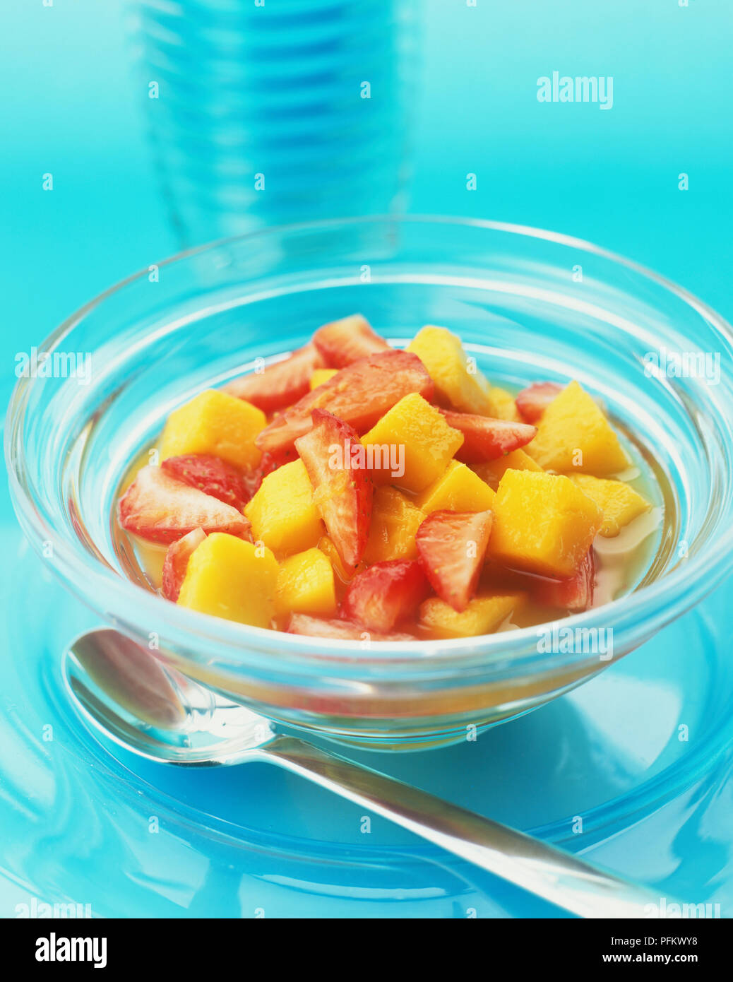 Obst Salat in einer Glasschale aus Erdbeeren und Mangos in Orangensaft, Zitronensaft und Honig. Eine silberne Dessert Löffel ist an der Seite der Schüssel. Stockfoto