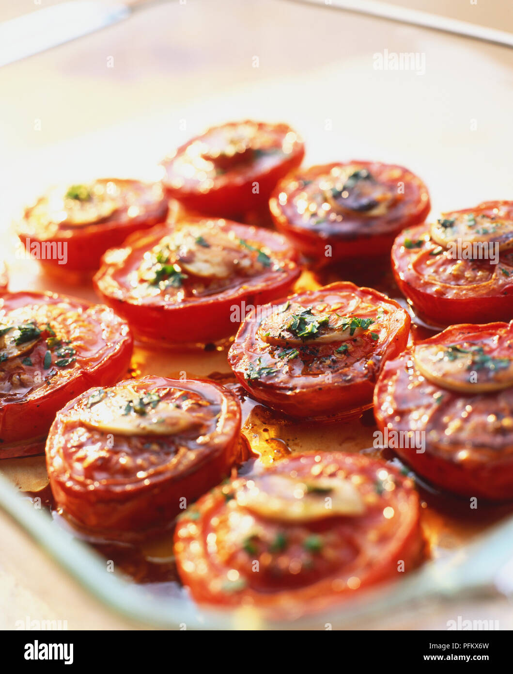 Langsam Braten Tomaten Salat, mit den Tomaten in ein Backblech mit einer Scheibe Knoblauch auf der Oberseite jeder Tomate, mit Salz und Pfeffer würzen und Kochen in Honig, Essig und Öl. Stockfoto