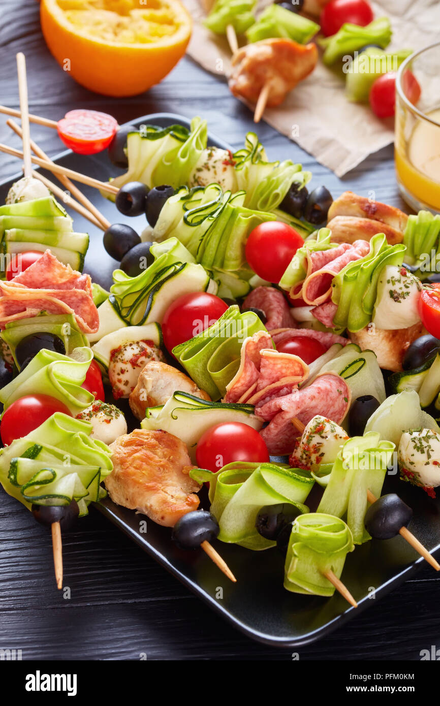 Zucchini ribbon Salat auf Spieße mit Hähnchenfleisch, Tomaten, Mozzarella Kugeln, Salami, Oliven auf einer schwarzen Platte auf einem Holztisch mit frischen Orange Ju Stockfoto