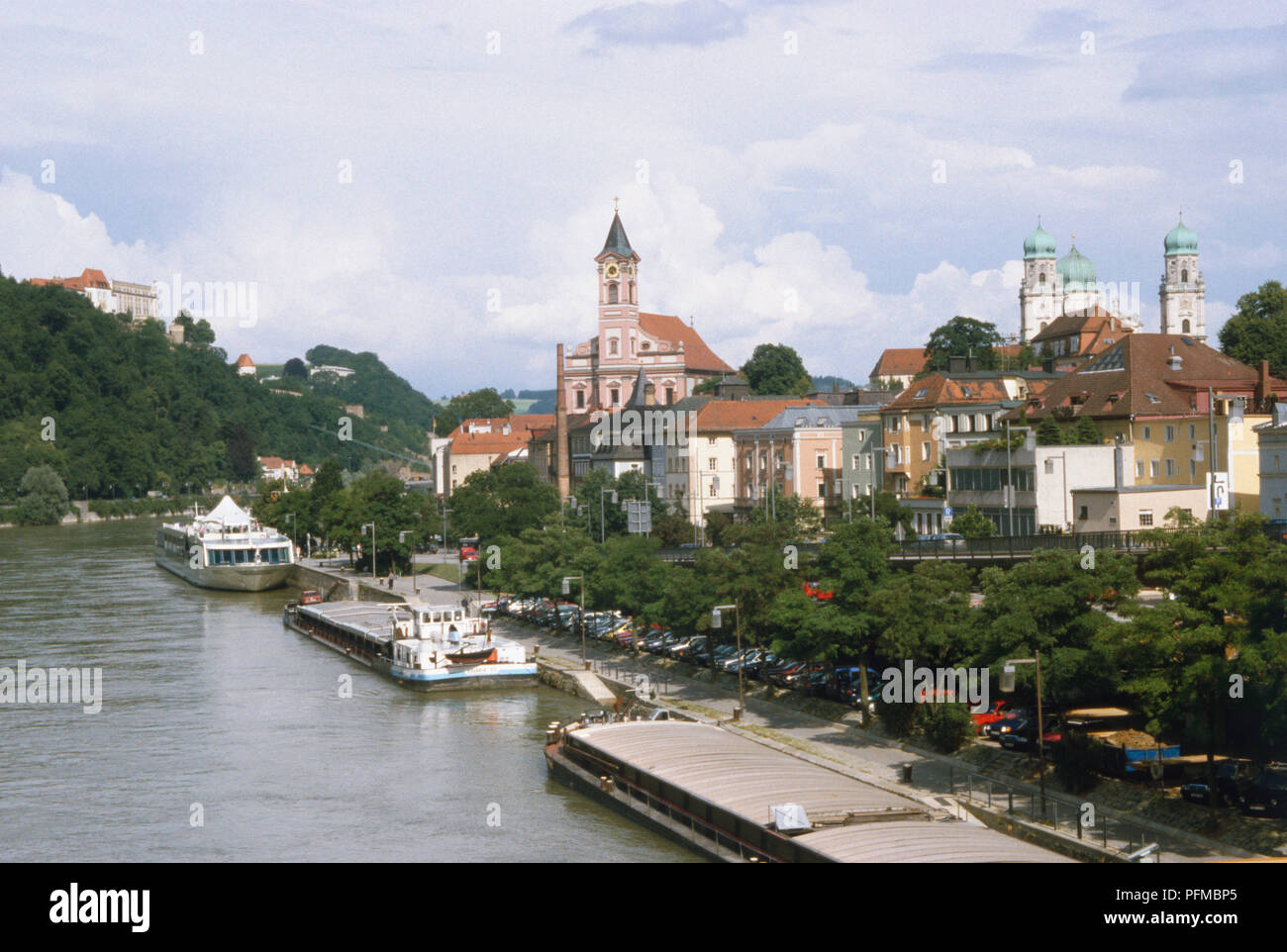 Deutschland, Bayern, der schönen Altstadt von Passau, an der Donau. Der Fluss ist mit industriellen Lastkähne gesäumt, die ein Passagier Schiff, mit den Zwiebeltürmen von Dom St. Stephan im Hintergrund. Stockfoto