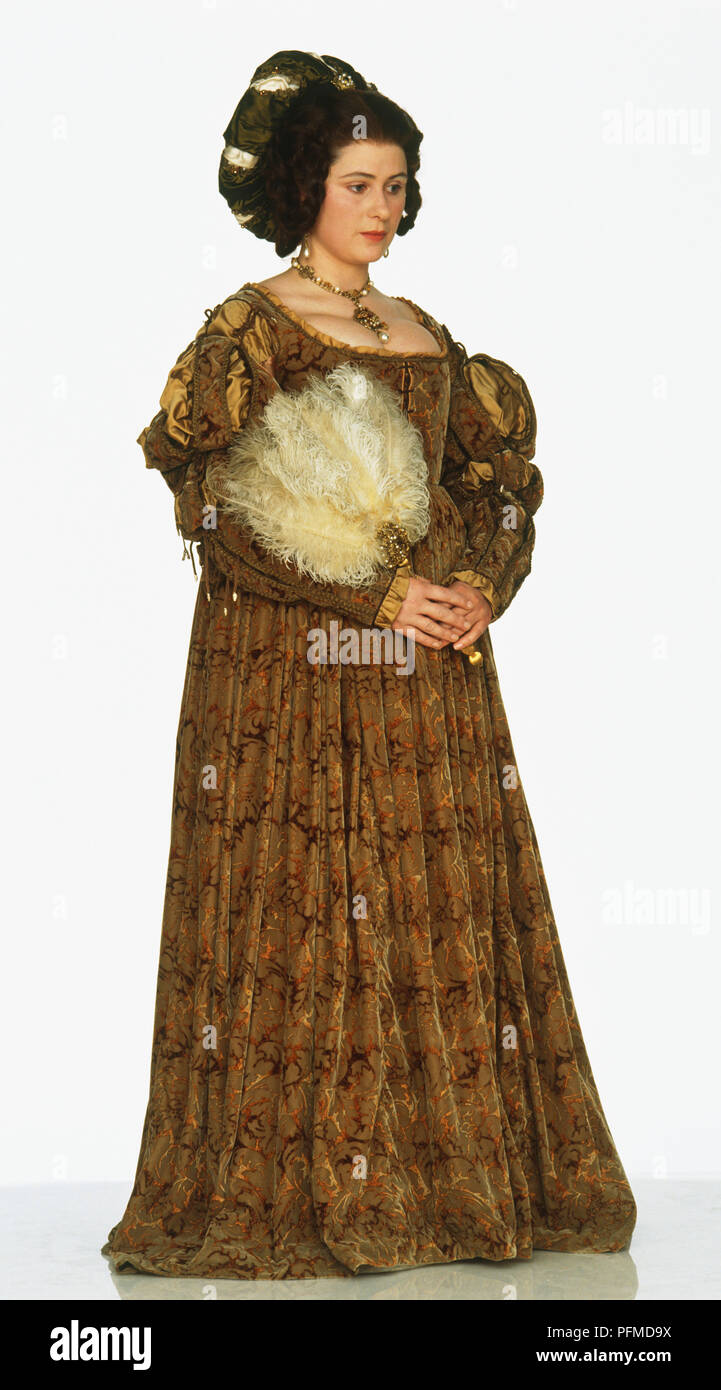Eine Frau trägt eine aufwändige Braun aus dem 15. Jahrhundert Stil Kleid,, einen Fächer aus Federn Stockfoto