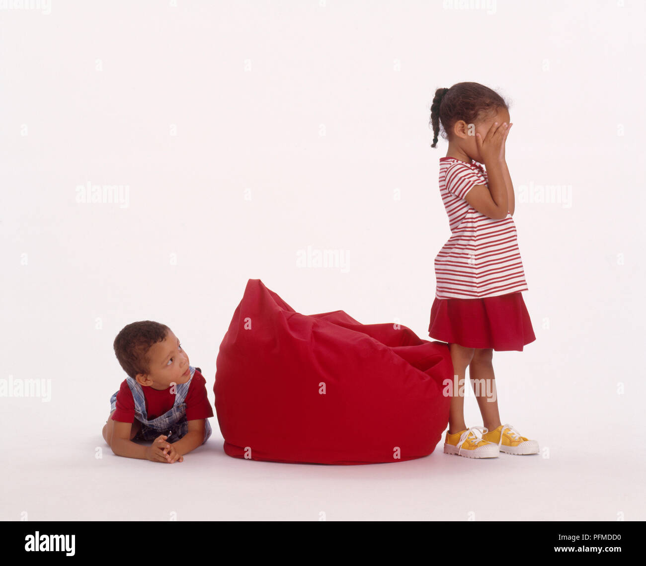 Junge versteckt sich hinter einem Bean Bag als Mädchen zählt mit ihren Kopf in ihren Händen, close-up Stockfoto