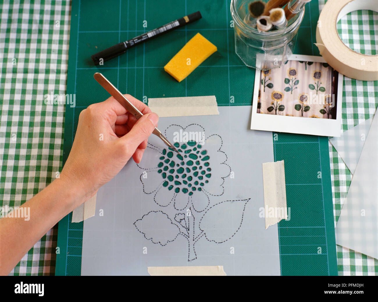 Sonnenblume Schablone über grüne Material angebracht, von Hand schneiden Sie kleine Löcher in der Mitte der flowerhead mit kleinen Metall Cuttermesser, grün und weiß karierten Tischtuch unter überprüft. Stockfoto