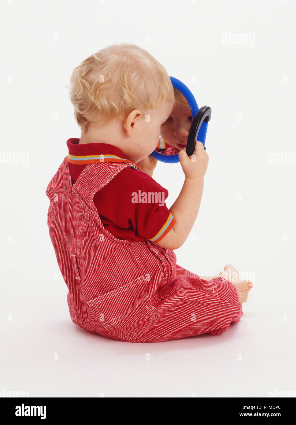 Baby Boy tragende rote Latzhose in einem Spiegel zu betrachten Stockfoto