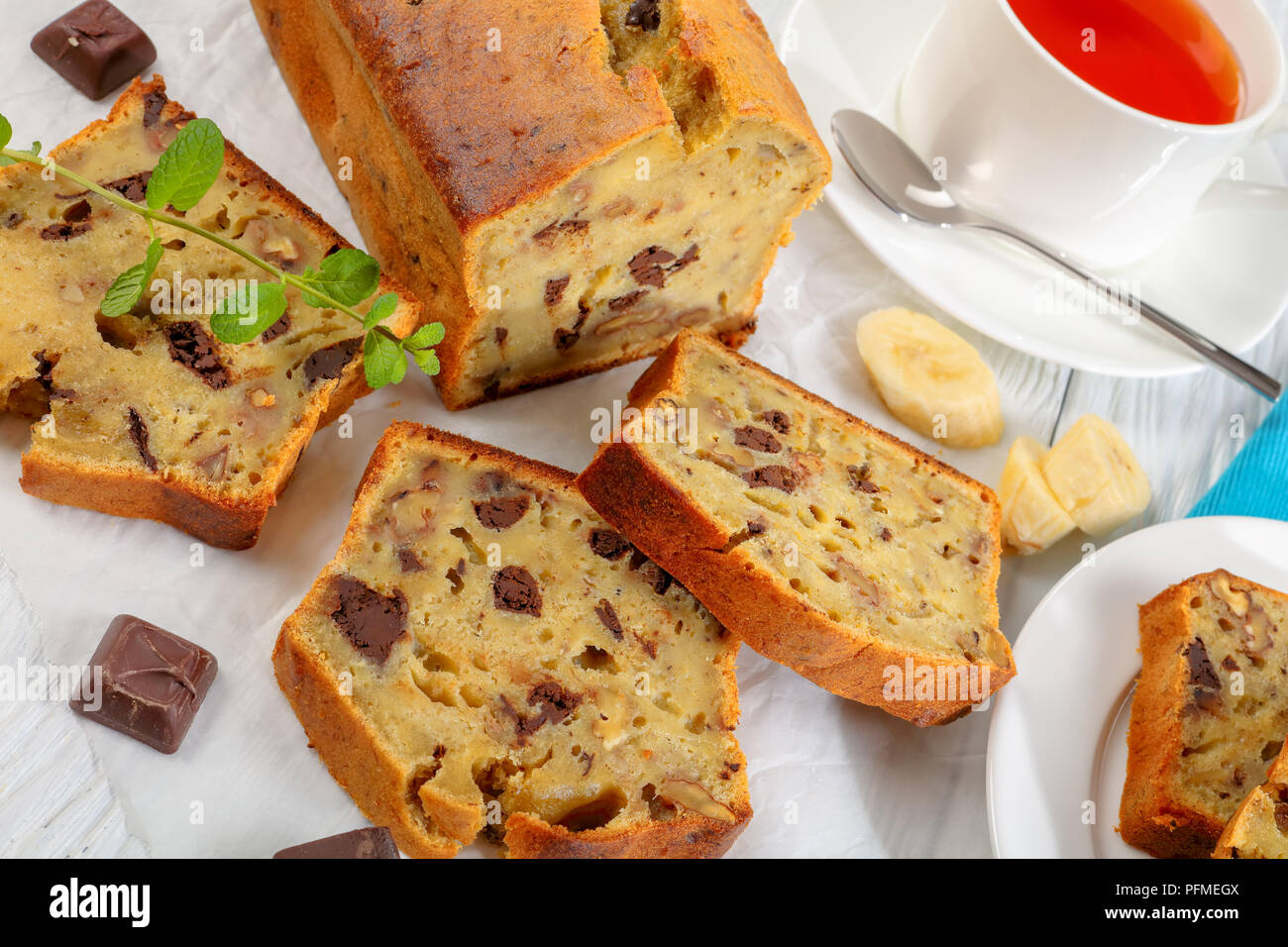 In der Nähe der frisch gebackene leckere Bananen Brot mit Nüssen und Schokolade Stücke in Scheiben schneiden auf Schneidebrett. Zutaten und Tasse Tee auf Woode Stockfoto