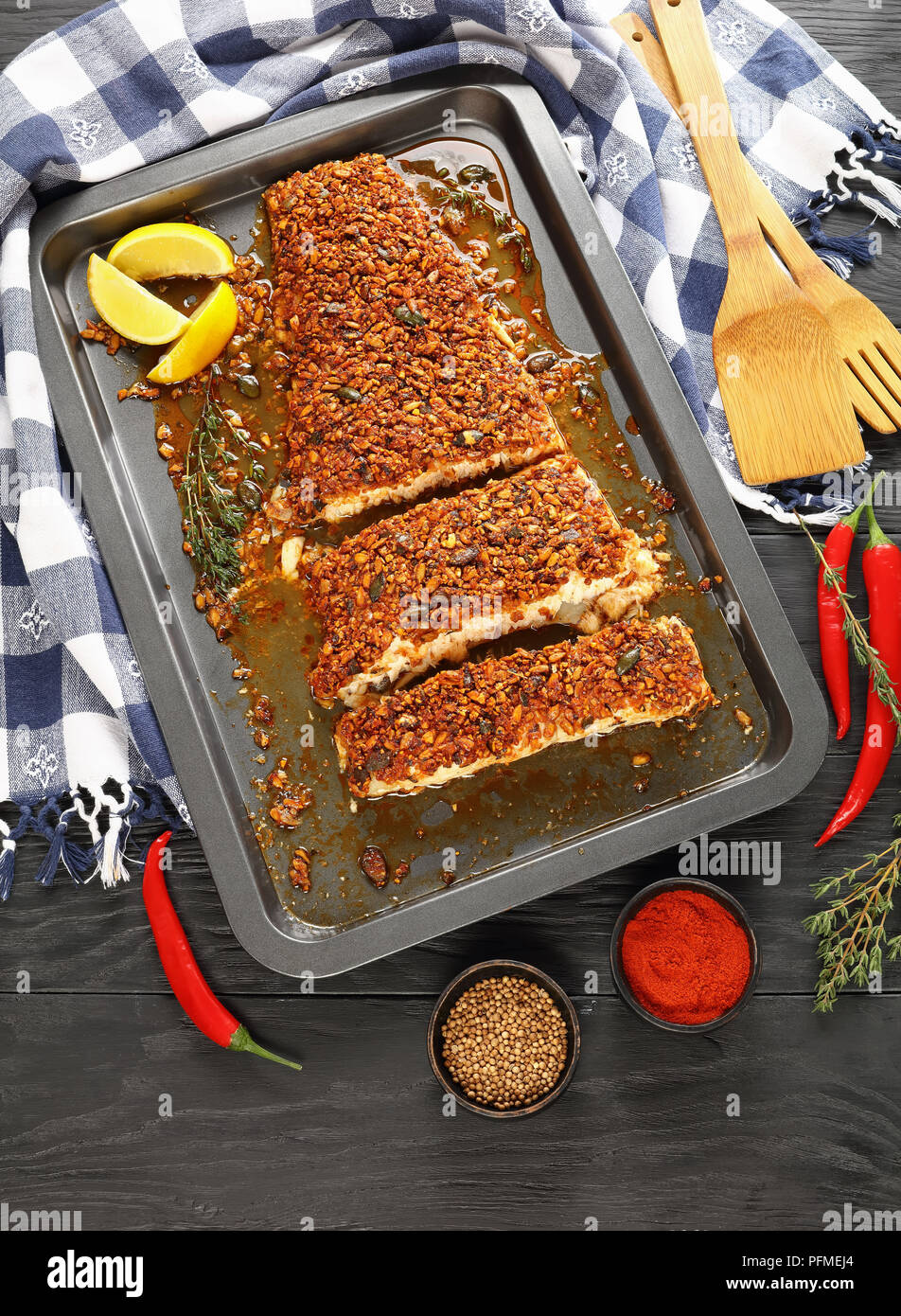 Kürbis, Sonnenblumen und Chili - Verkrusteten Fischfilet auf Backblech mit Küchentuch, Spatel und Zutaten auf Holztisch, vertikale Ansicht her Stockfoto