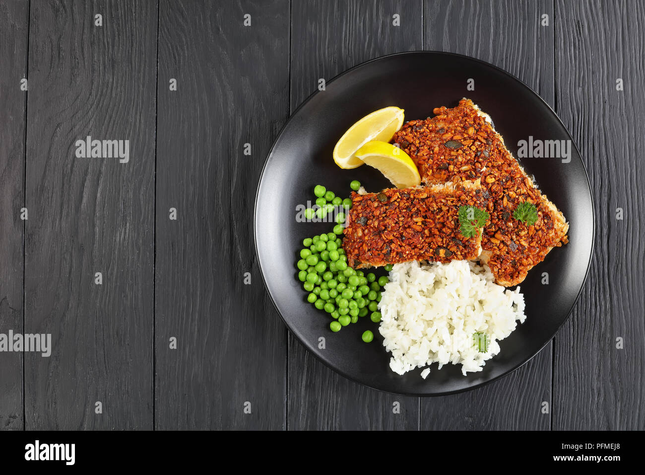 Kürbis, Sonnenblumen und Chili - Verkrusteten Fischfilets, serviert mit Reis und Erbsen auf schwarze Platte, Ansicht von oben Stockfoto