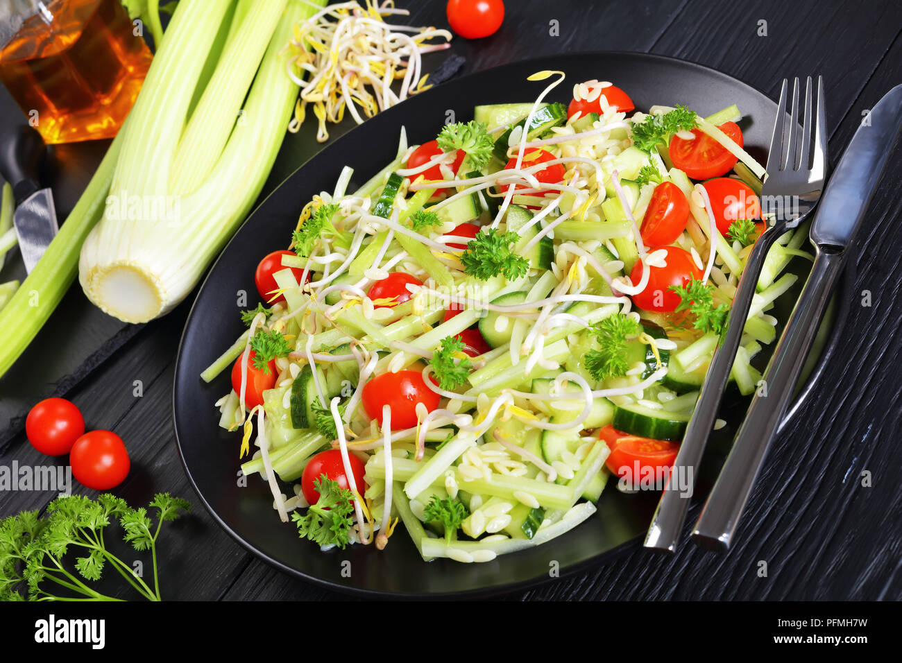 Köstliche frische Pasta Salat mit Gurkenscheiben, Selleriestangen, Tomate und Sojasprossen auf schwarze Platte auf schwarzer Holztisch mit Sesamöl und Ingr Stockfoto