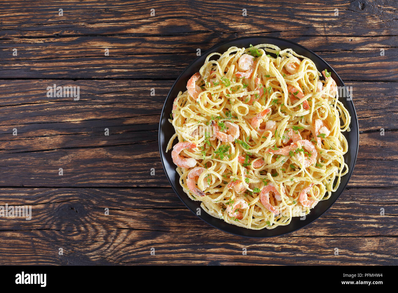 Köstliche cremige Parmesan Linguine mit Shrimps bestreut mit fein gehackter Petersilie auf schwarze Platte auf Holz rustikal Tisch, horizontale Ansicht von abov Stockfoto
