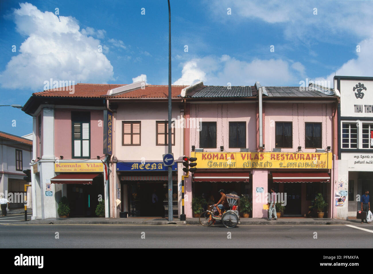 Singapur, Little India, die Reihe von Restaurants und Geschäften, lackiert rosa und weiß, Fensterläden, Markisen über shop Fronten, rote Ampel, Radfahrer, Fußgänger auf der Rikscha vorbei gehen. Stockfoto