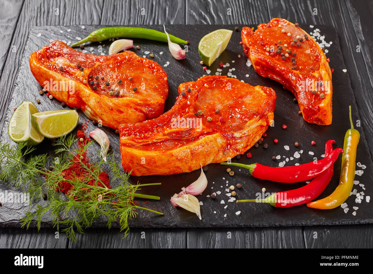 In der Nähe von roh marinierte Schweinekoteletts vorbereitet zu kochen, mariniert mit Gewürzen und roten sriracha Soße auf schwarzem Schiefer Fach mit Chili Pfeffer, Salz, Kalk Stockfoto