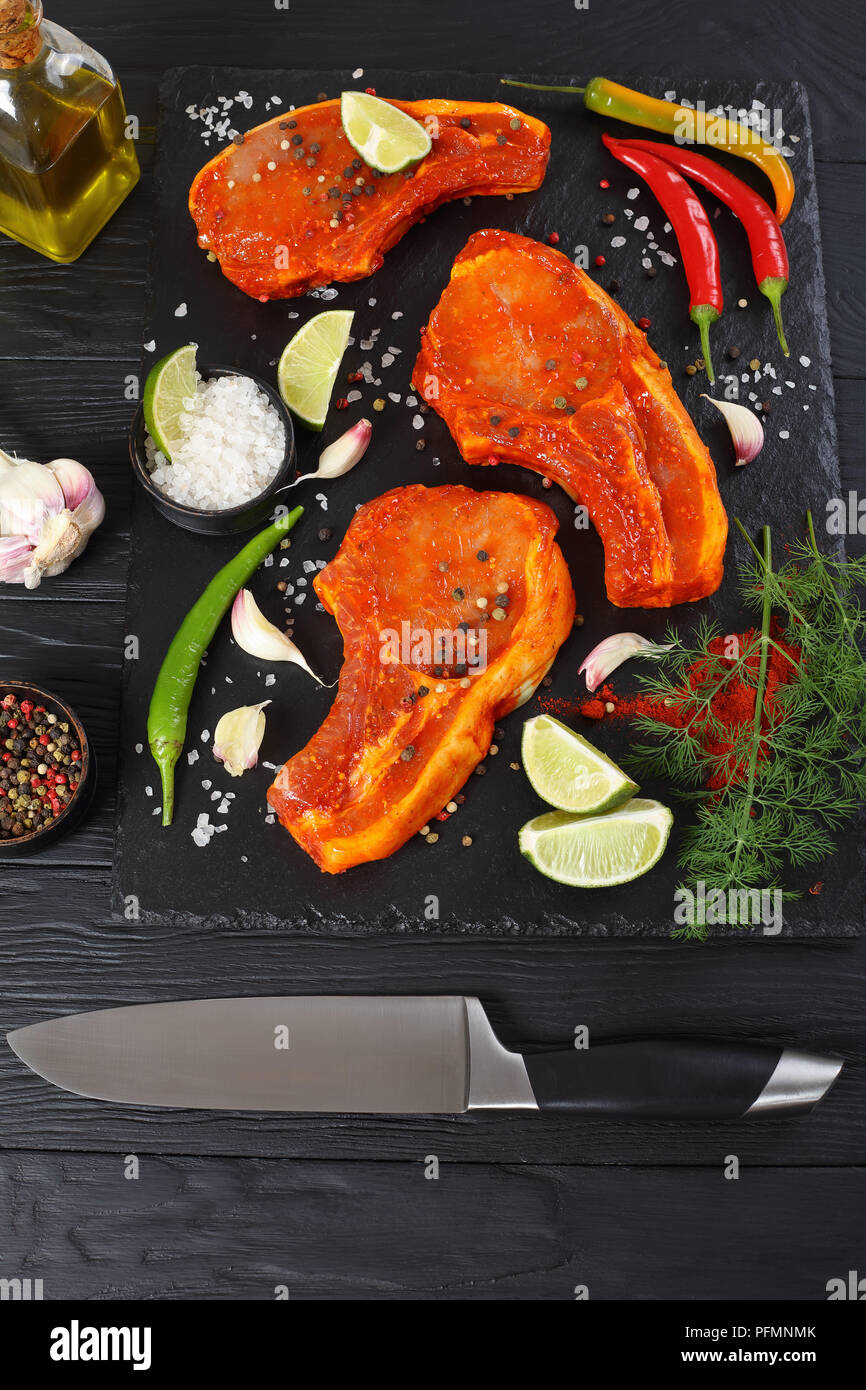 Rohe Schweineschnitzel vorbereitet zu braten, mit Gewürzen und roten sriracha Soße auf schwarzem Schiefer Fach mit Chili Pfeffer, Salz, Kalk Schichten und Gewürze o Marinierte Stockfoto