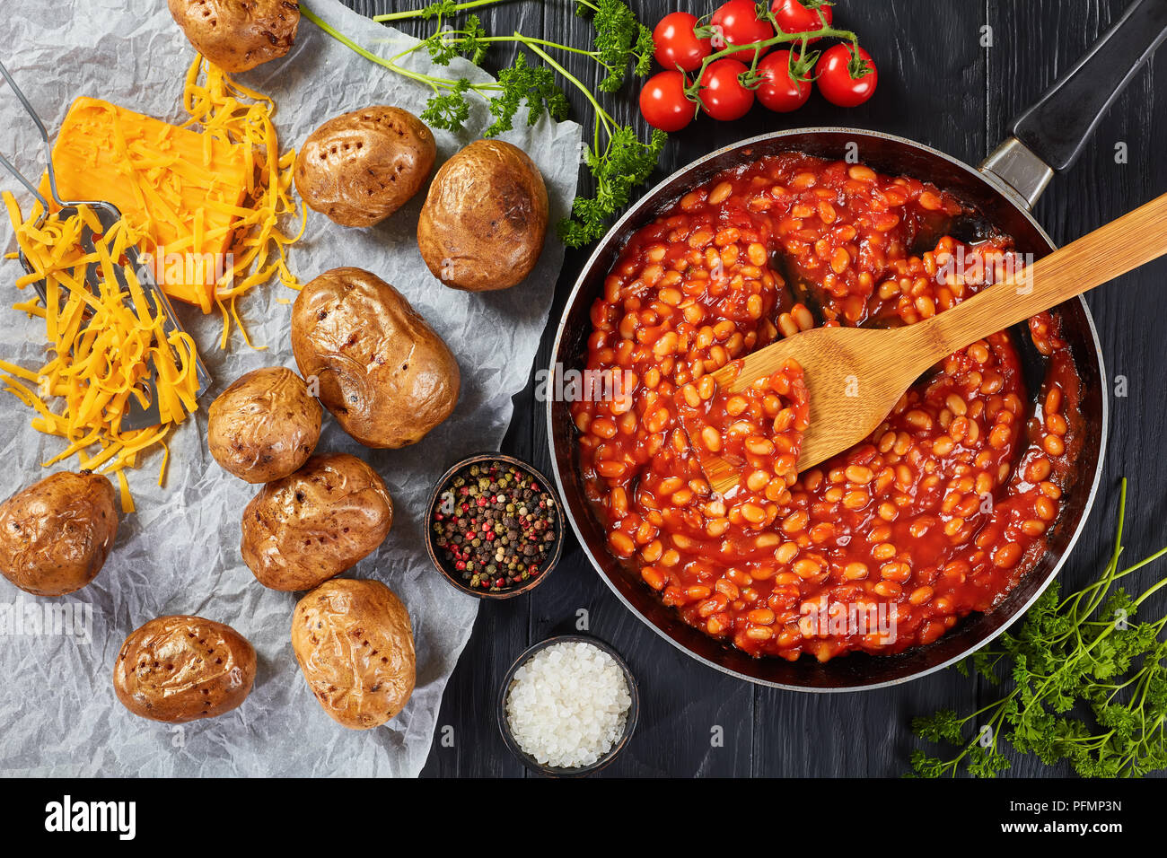 Bohnen mit Tomatensauce in einer Pfanne. gebackene Kartoffel oder Pellkartoffeln mit Goldgelb knusprige Haut auf einem Papier mit Cheddar Käse im Hintergrund, Anzeigen Stockfoto