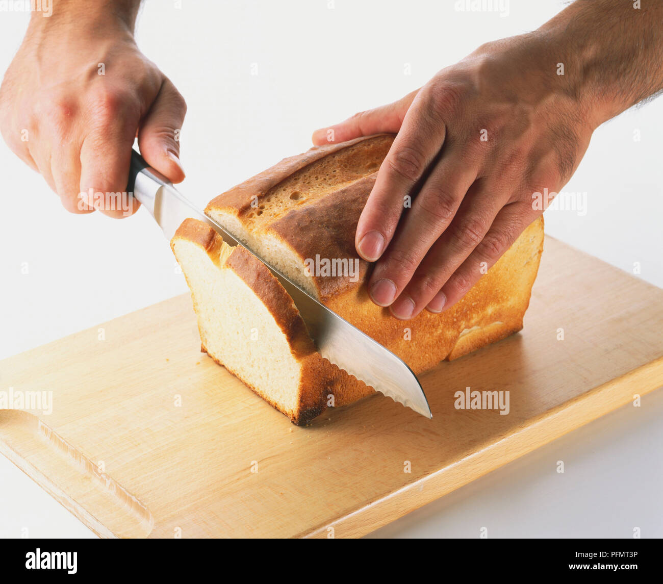 Nahaufnahme der Slicing ein Laib Weißbrot mit einem scharfen Brotmesser mit Wellenschliff. Stockfoto