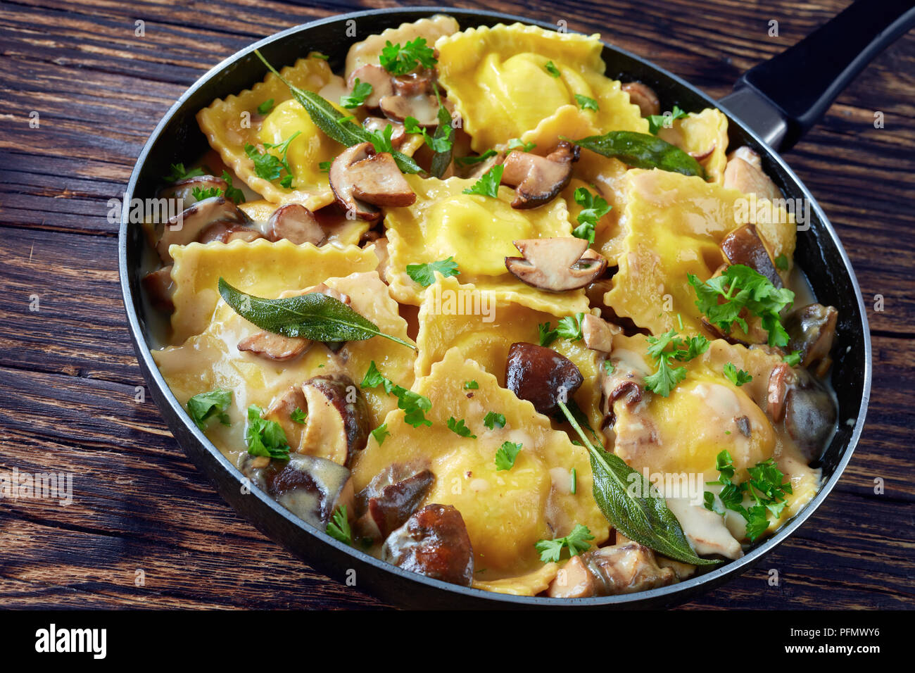 Leckere Ravioli gefüllt mit Ricotta in cremiger Sauce Knoblauch Pilze in einer Pfanne auf einem alten Holztisch gekocht, Ansicht von oben, close-up Stockfoto