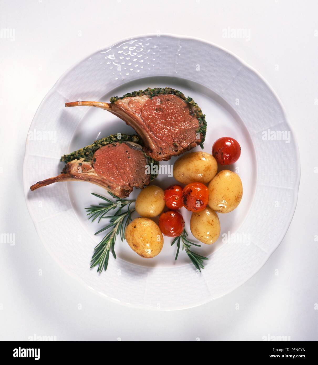 Rack mit Lammkoteletts serviert auf Platte mit neuen Kartoffeln, Tomaten und Rosmarin Stockfoto